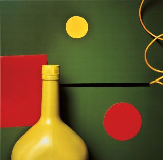 A yellow bottle against a green wall with red dots