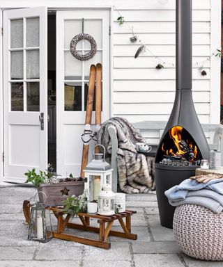 Christmas porch decor ideas with white shiplap walls, a black chiminea, wooden skis and fur and wool blankets on seats