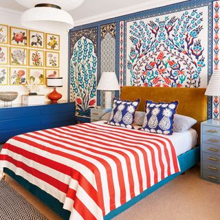 Master bedroom with feature wall of colourful patterned wallpaper and red and white striped bedspread