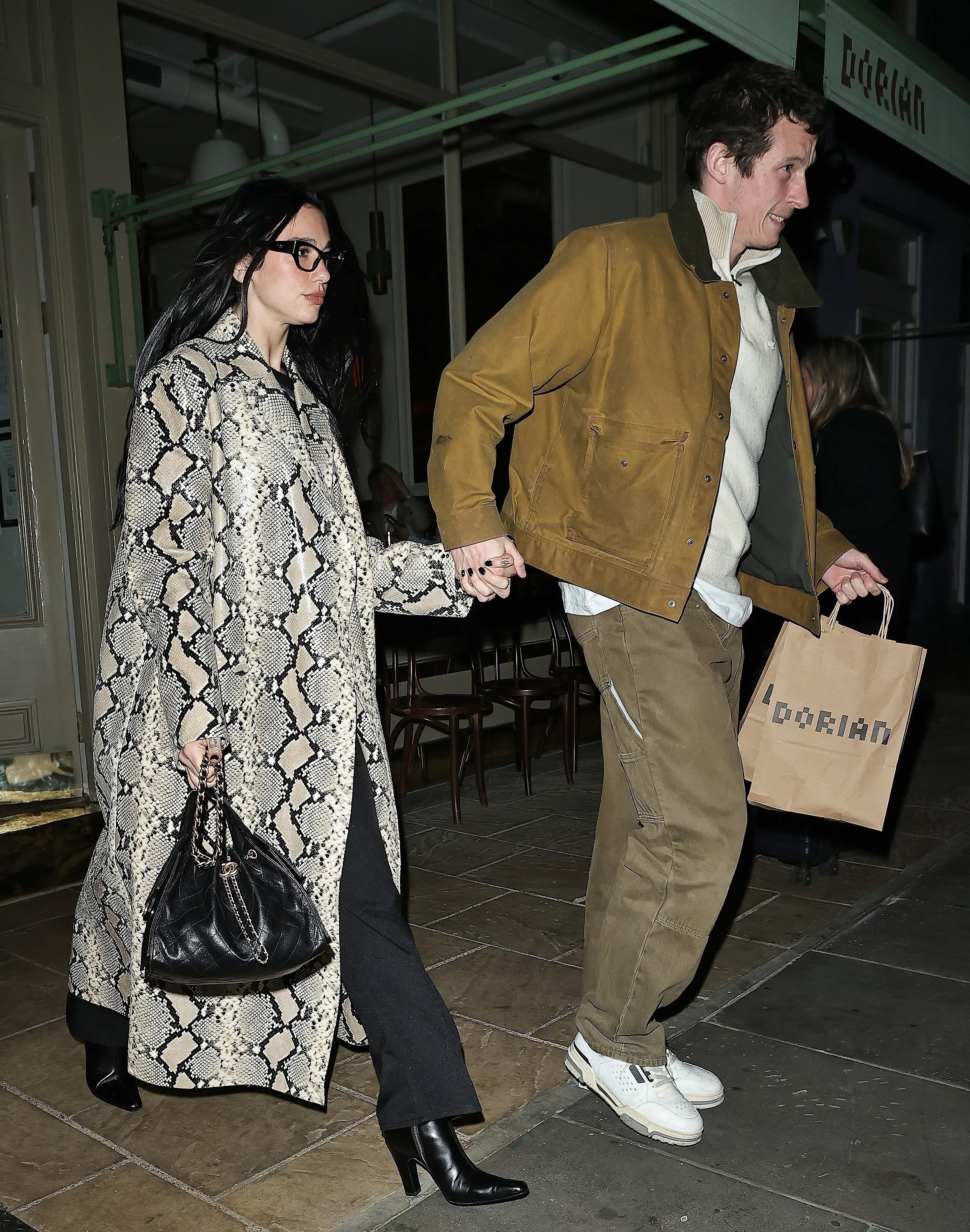 Dua Lipa holds hands with rumored fiance Callum Turner while wearing a snakeskin trench coat and carrying a Chanel 25 handbag