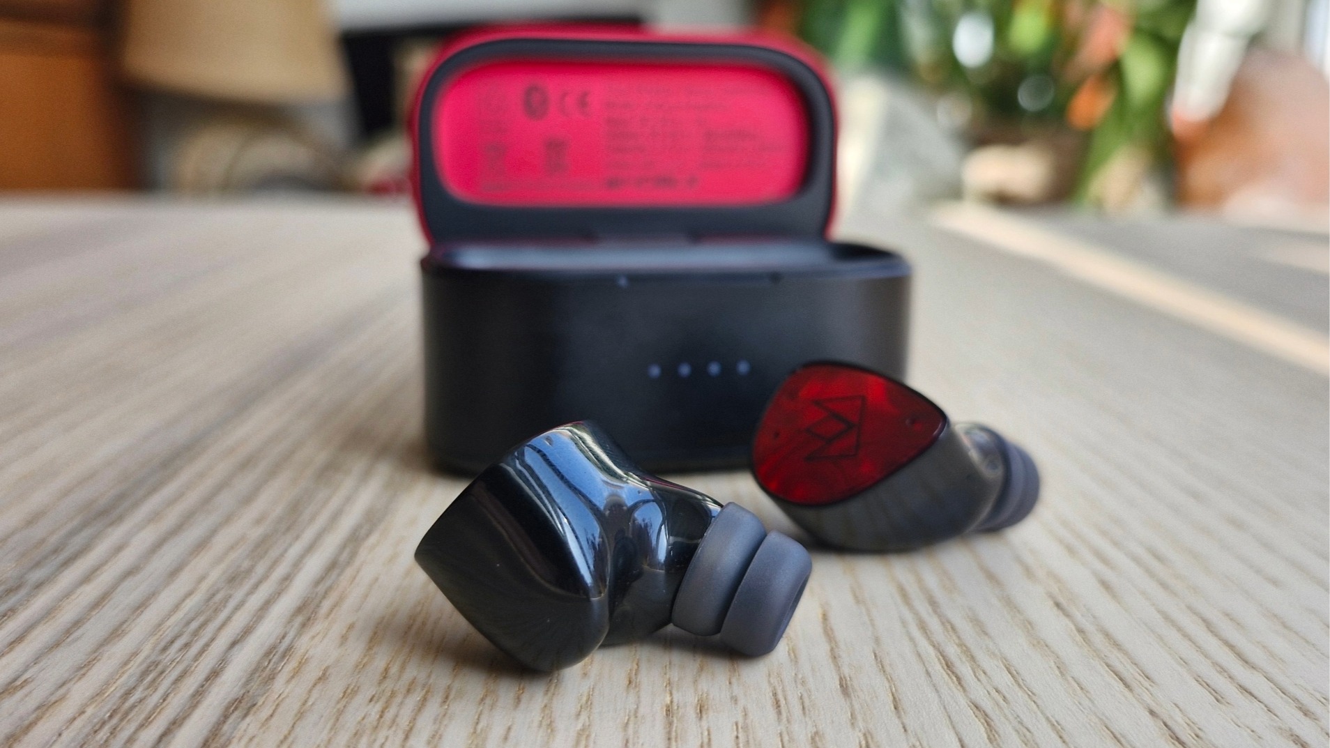 Noble FoKus Amadeus in-ear earbuds in front of their carry case on a wooden surface