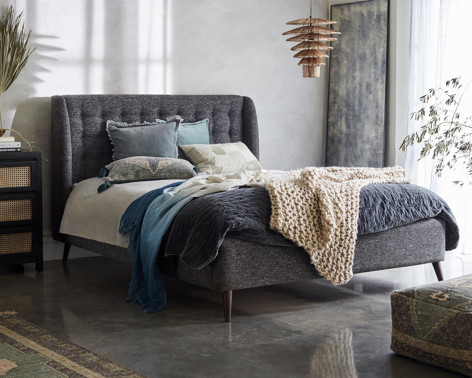 A large bedroom containing DFS X French Connection Camden King bed frame, rattan chest of drawers, hanging pendant light fixture and plush ottoman