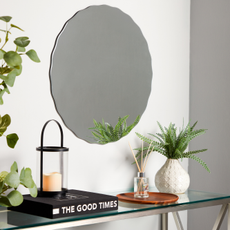 scalloped mirror aover glass shelf with house plants and The Good Times book