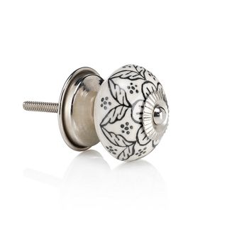 An ornate white door knob with a black floral design