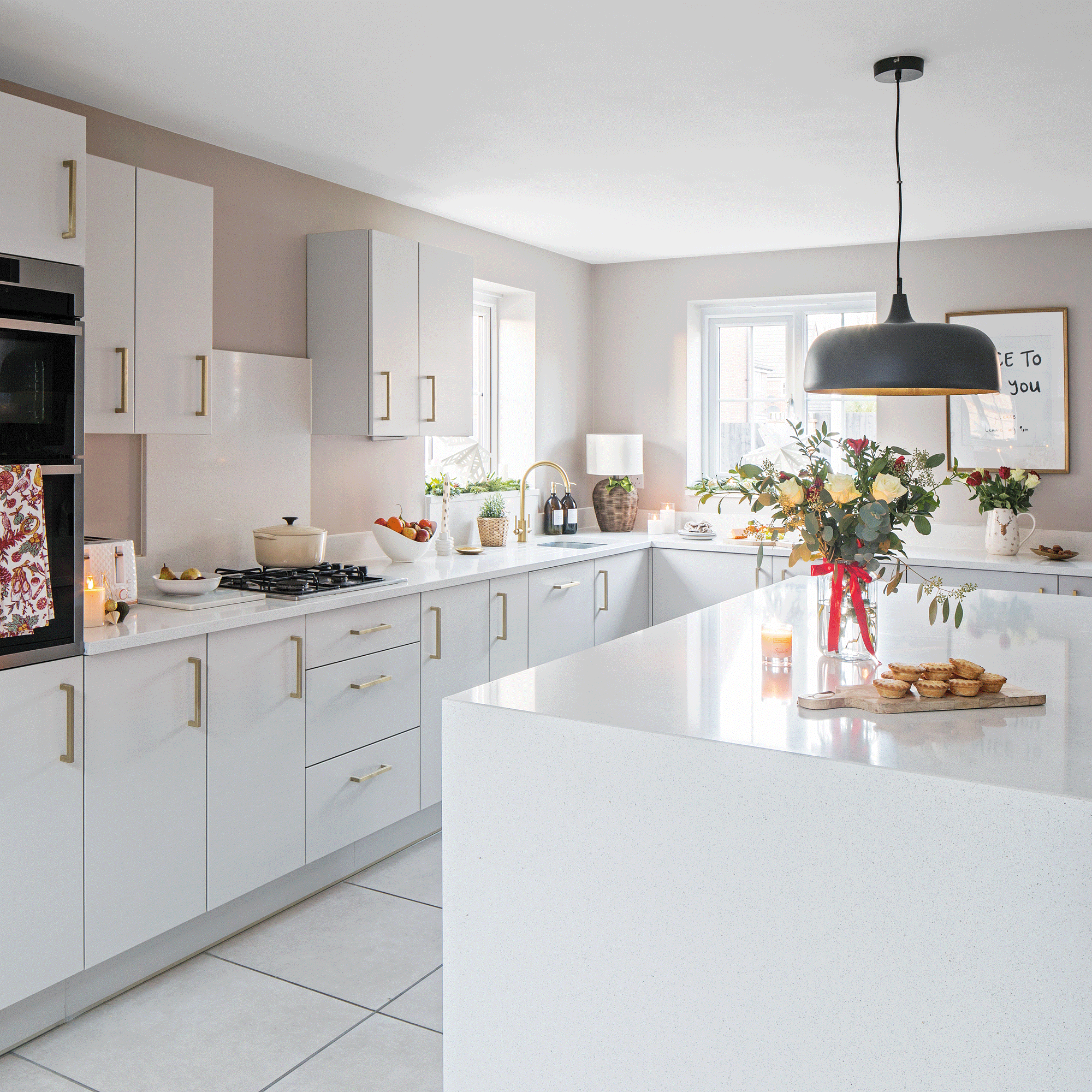 a white contemporary kitchen with a black pendant over an island and festive decorations