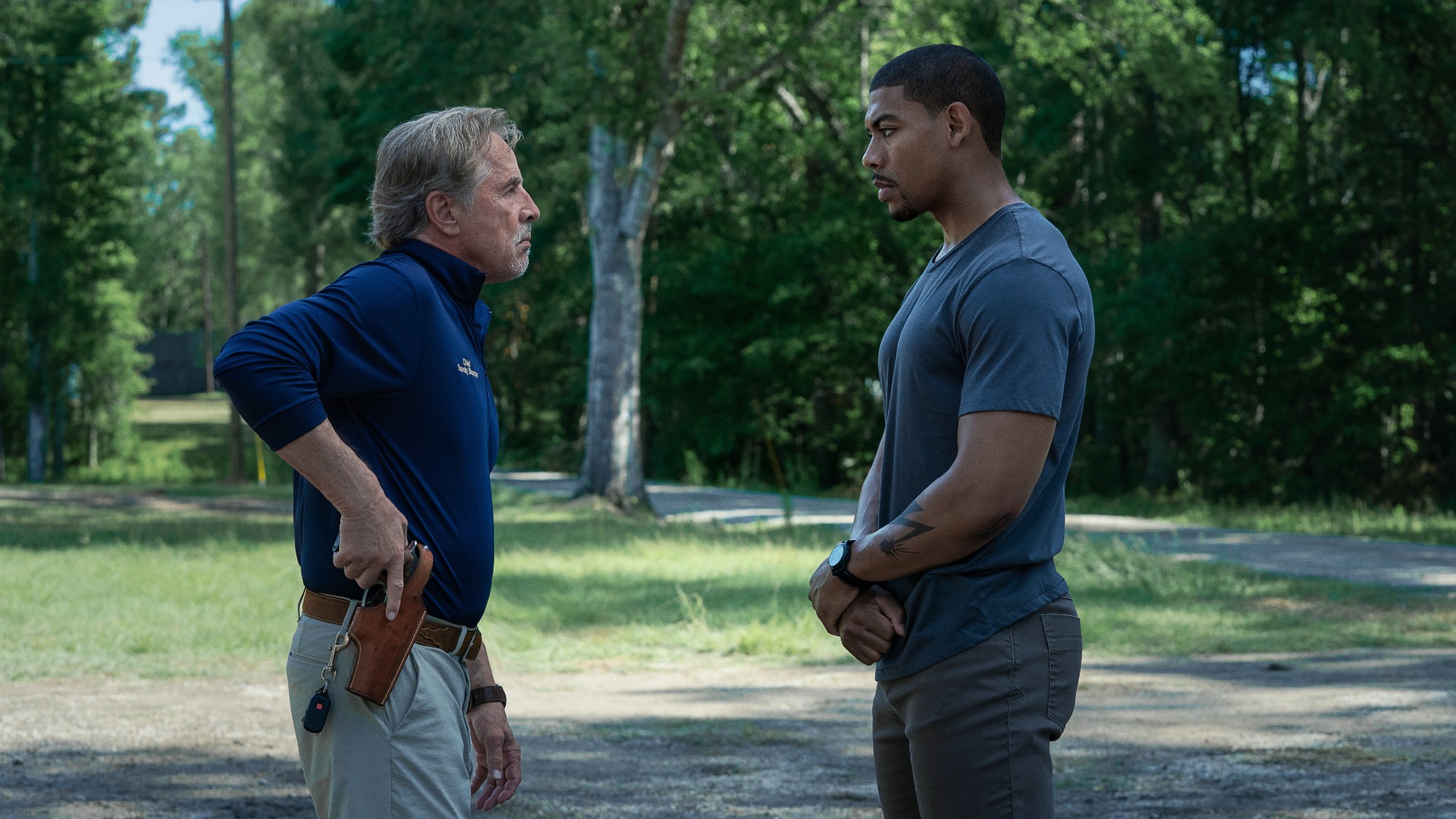 Don Johnson reaching for a gun as he stands face to face with Aaron Pierre in a green space in the movie "Rebel Ridge"