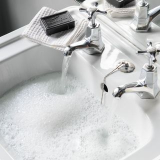 A water-full bathroom sink with a running tap