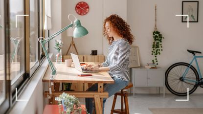 Woman smiling using one of the best productivity apps, sitting at a wooden desk with large lamp overhead in a home office