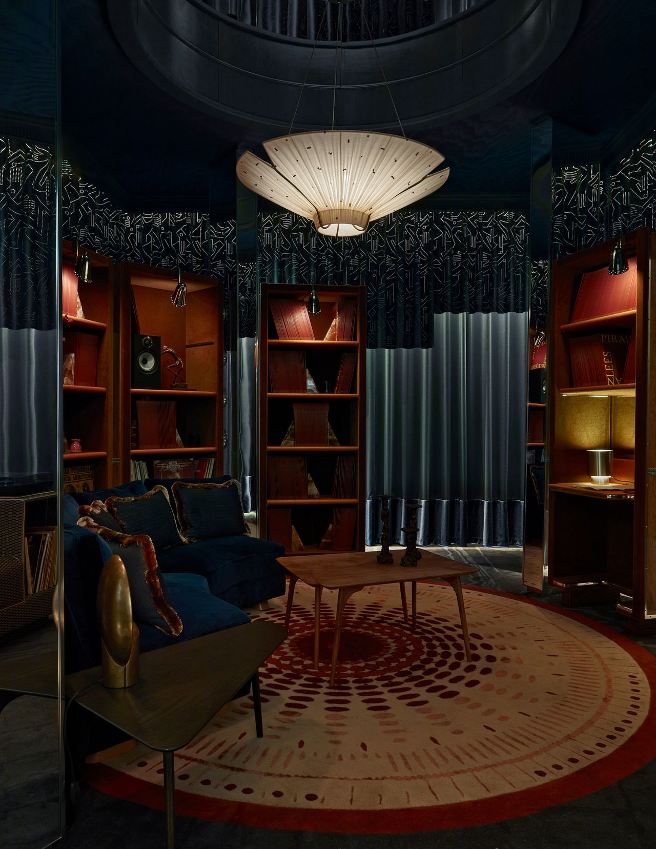 dedar library at wowhouse with round rug, bookshelves, floating pendant light, coffee table, curved couch, and curtains around the walls, including a perforated curtain detail