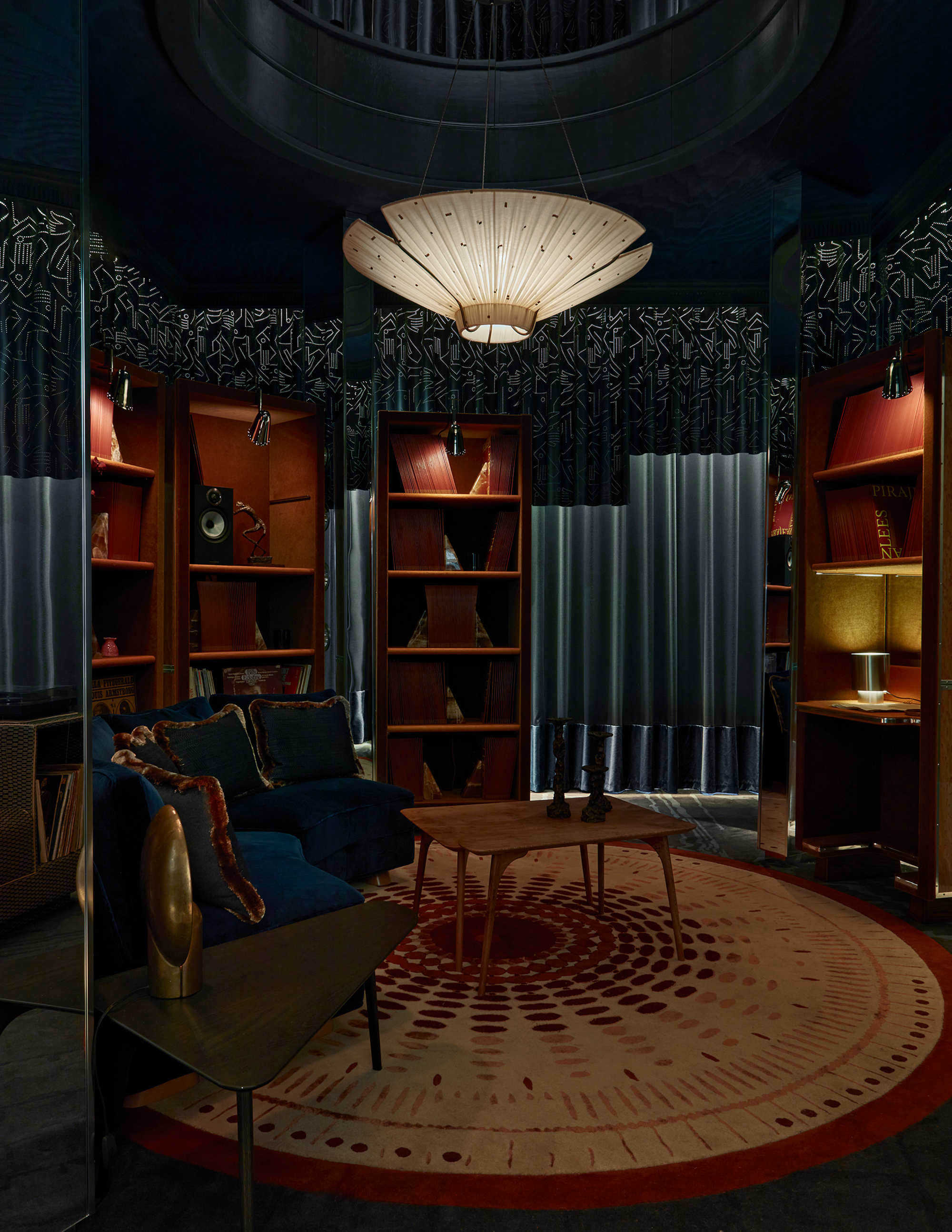 dedar library at wowhouse with round rug, bookshelves, floating pendant light, coffee table, curved couch, and curtains around the walls, including a perforated curtain detail 