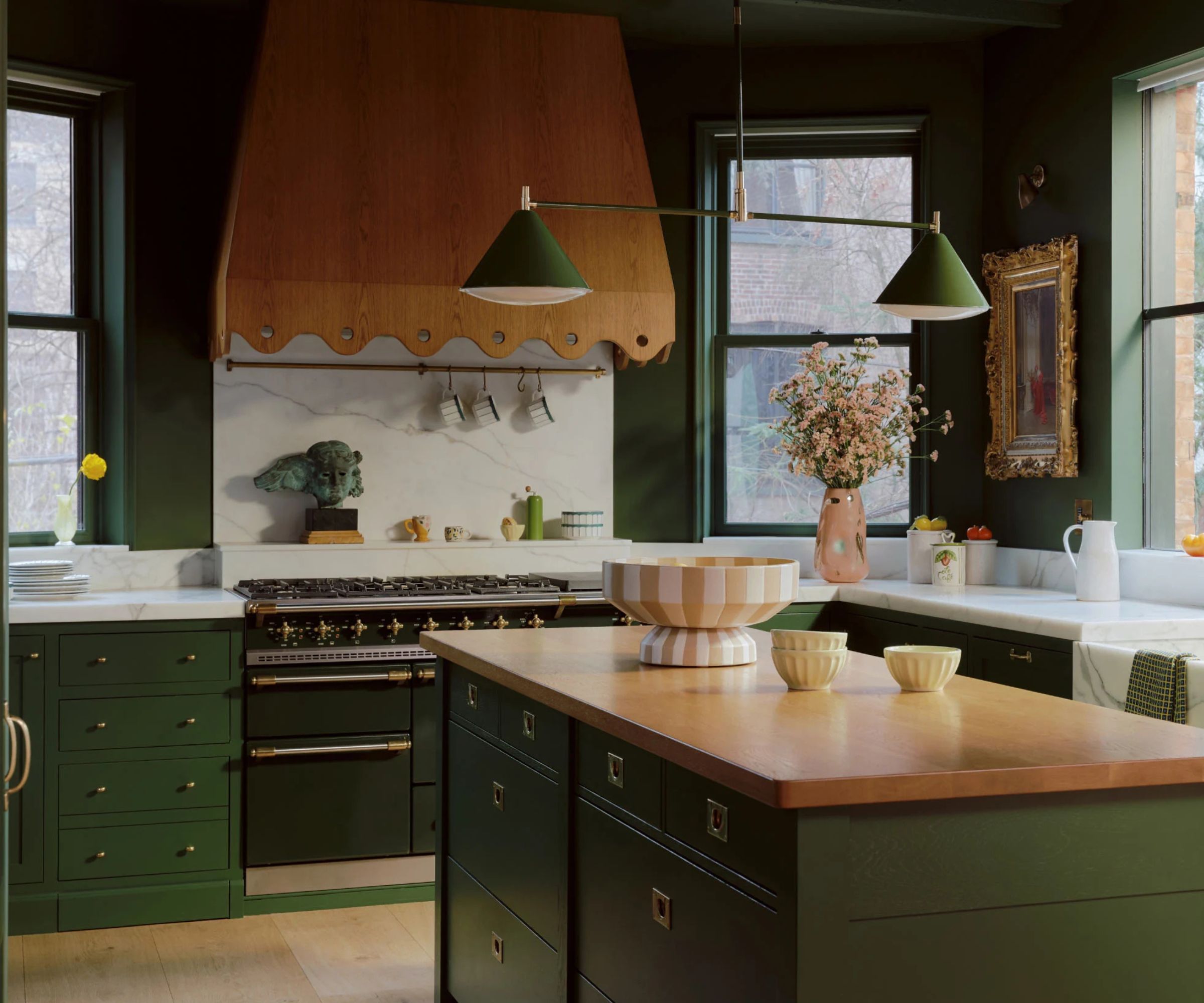 Anthropologie green kitchen with brass hardware and a wooden range hood