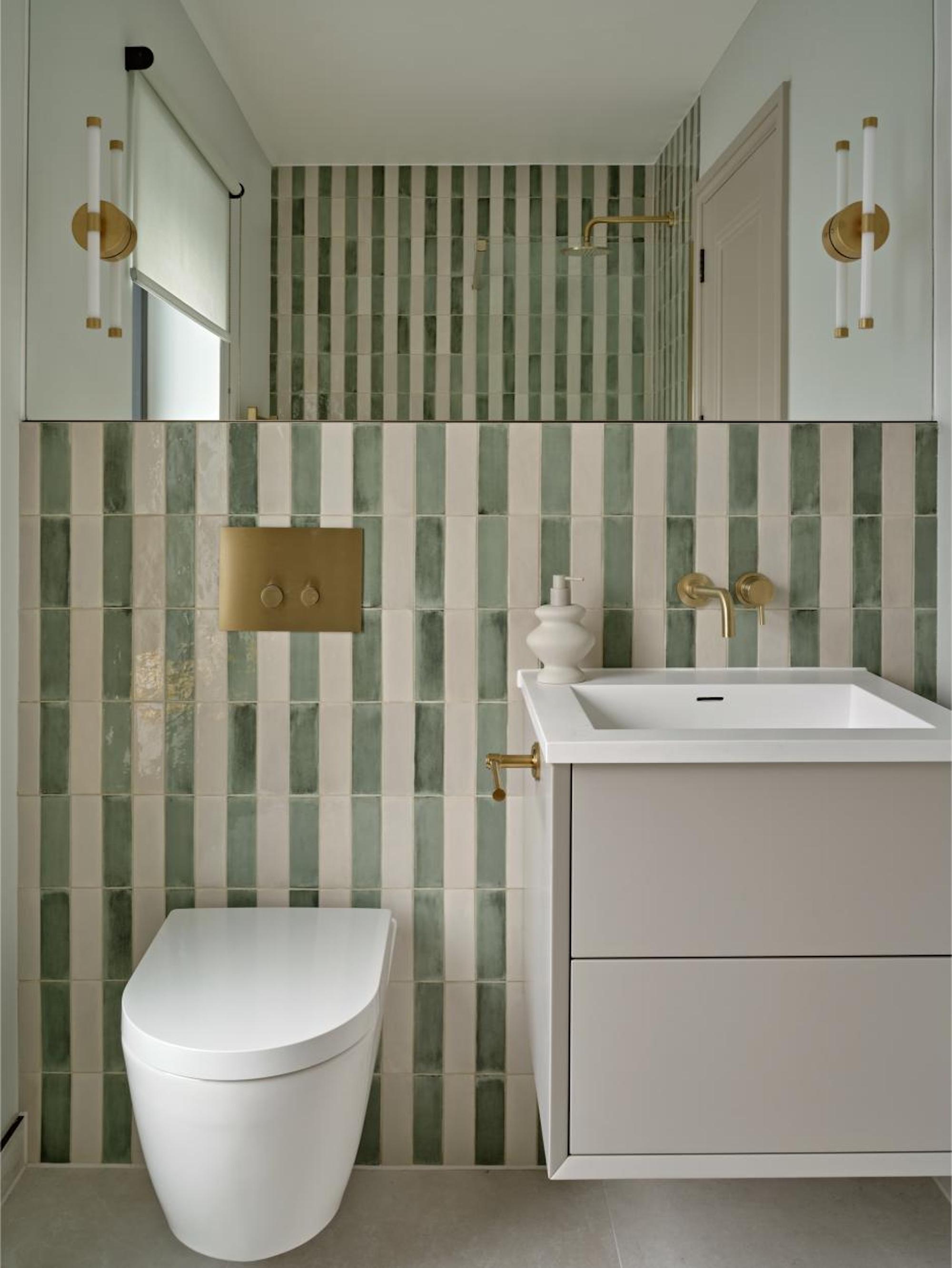 A modern en suite bathroom with cream and mint tiled wall with gold tapware and a large mirror above the sink.