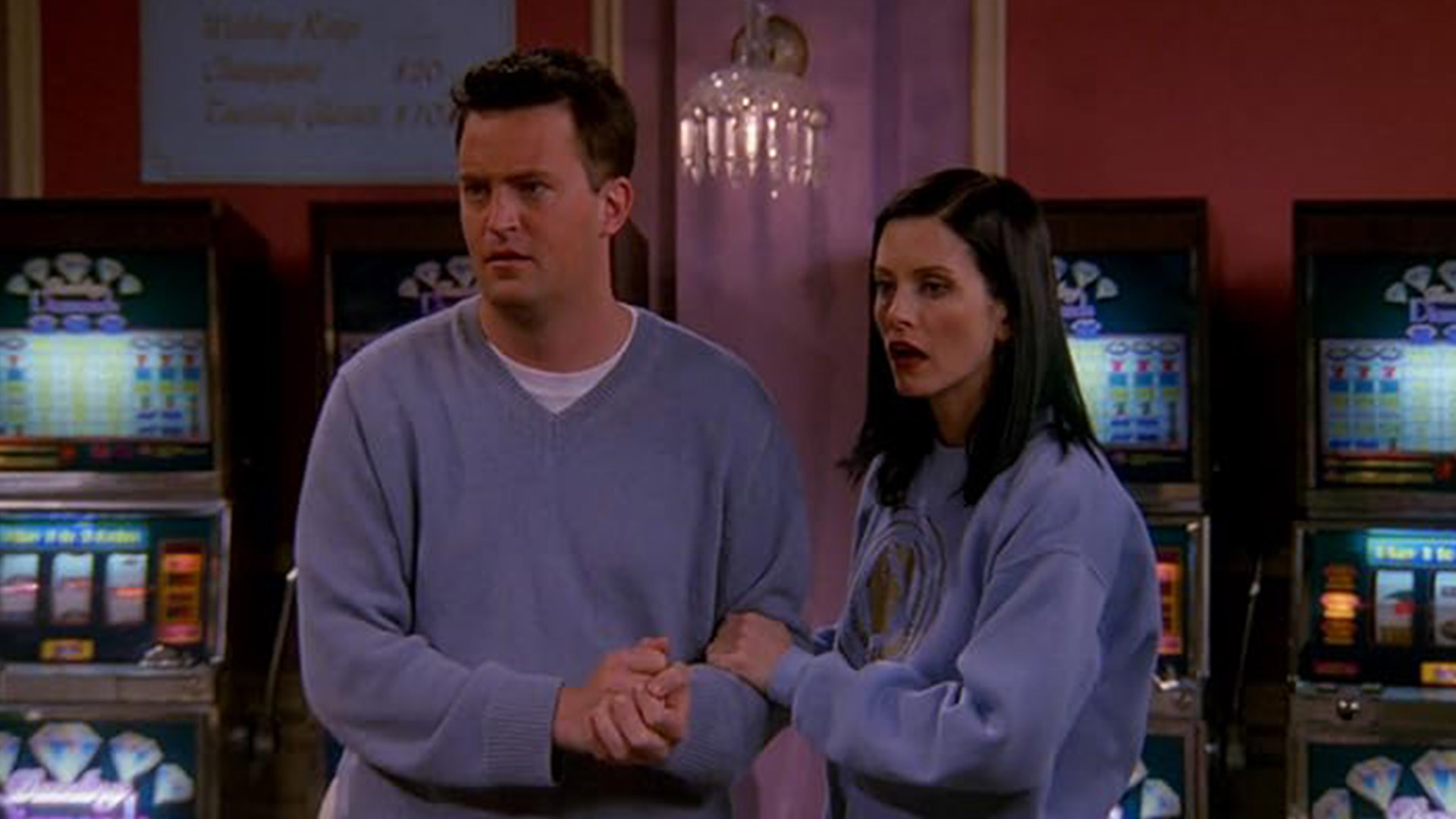 Monica and Chandler hold hands in the apartment of Friends