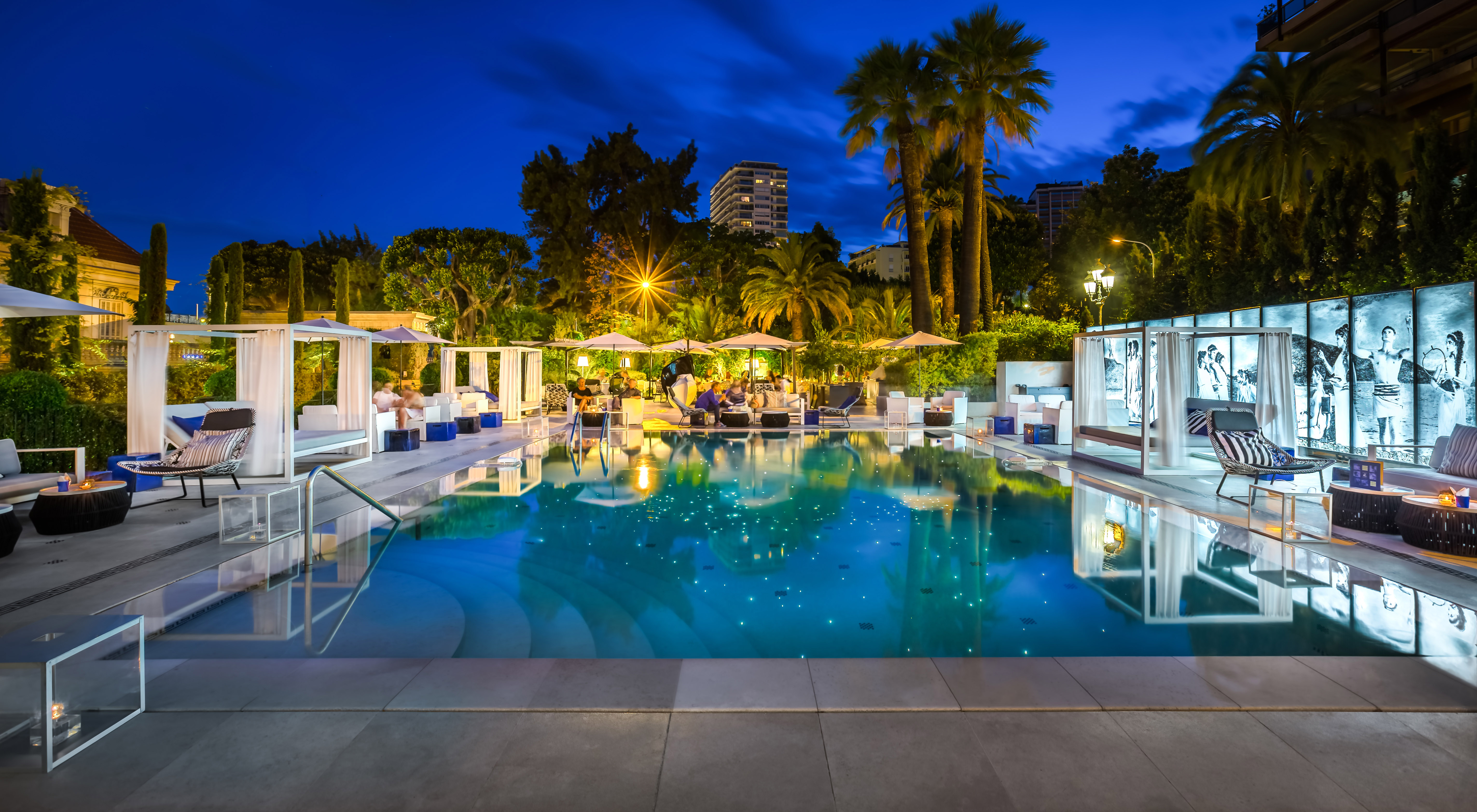 Square swimming pool, surrounded by sun beds, at nightime