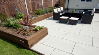 Contemporary garden with furniture and flowerbeds on light coloured patio slabs