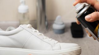 A white sneaker with a protection solution being sprayed on