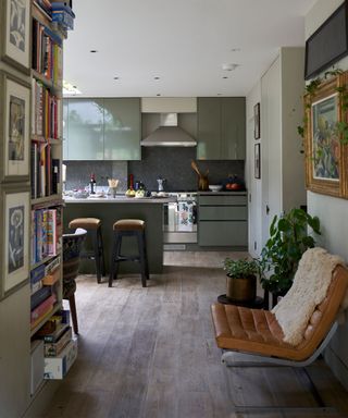 Inviting entrance to the kitchen with artwork on walls, shelves with books and board games, looking through to kitchen with green cabinets, kitchen island