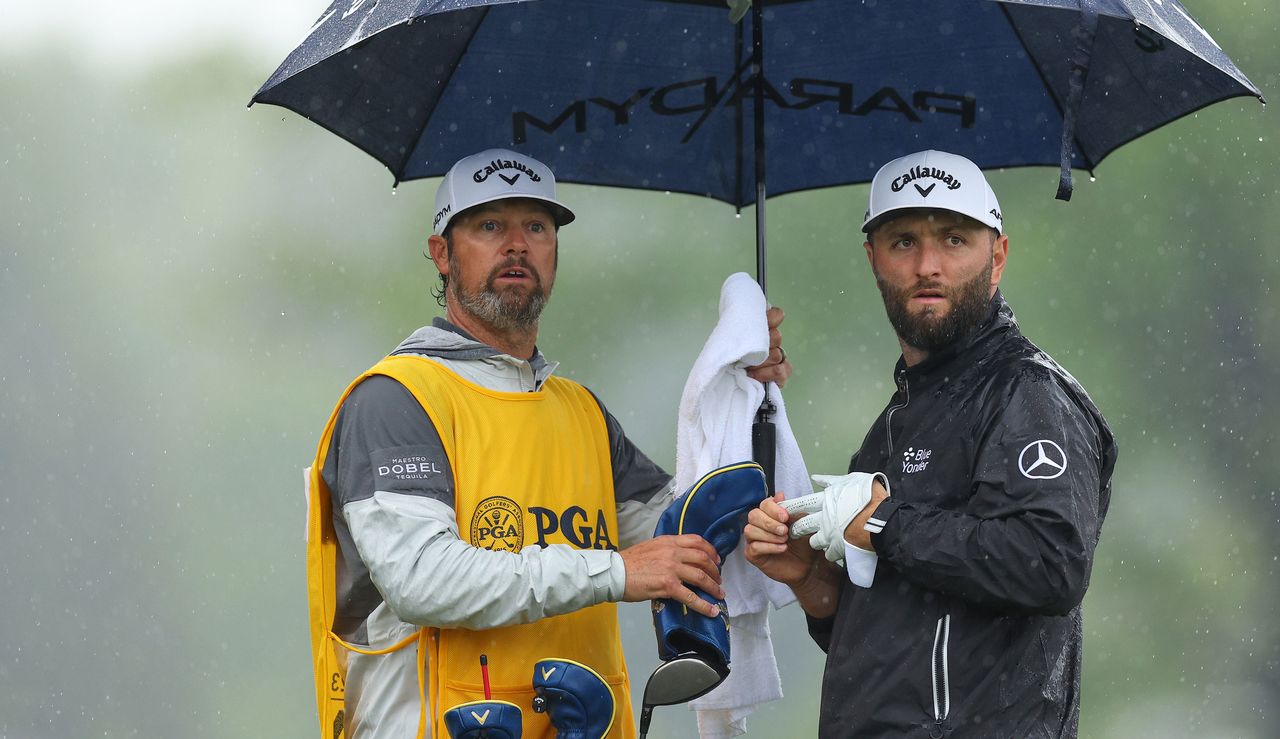 Jon Rahm talks to his caddie under an umbrella 