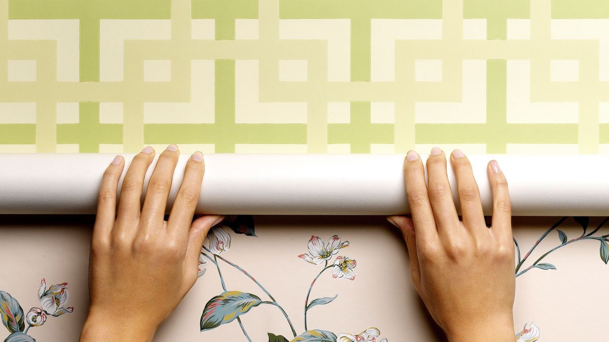 Hands on wallpaper roll over top of wallpaper on wall