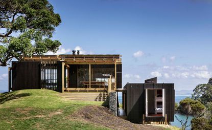 Exterior view of the retreat. Set on the shore, we see the ocean in the distance. The house is made out of multiple levels which are connected, and built mostly of natural materials, like wood. 