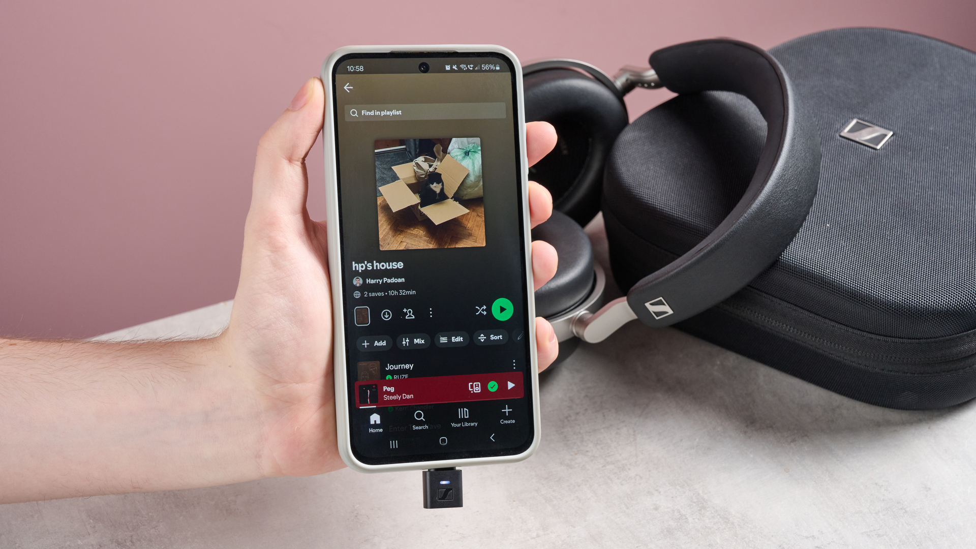 Person holding up phone with Spotify on in front of Sennheiser HDB 630 and carry case