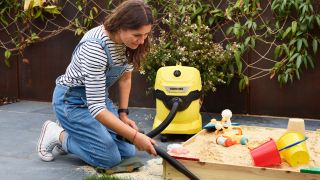 A woman using a Karcher WD3 to vacuum up sand from a kids sandbox