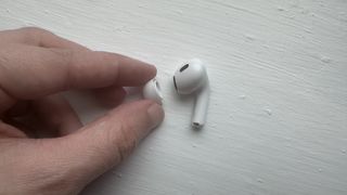 Apple AirPods Pro on a white surface with a new ear tip next to them.