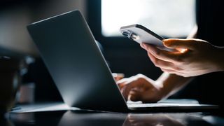 Close-up shot of a woman using mobile device with Two-Factor Authentication (2FA) security while logging in securely to her laptop.
