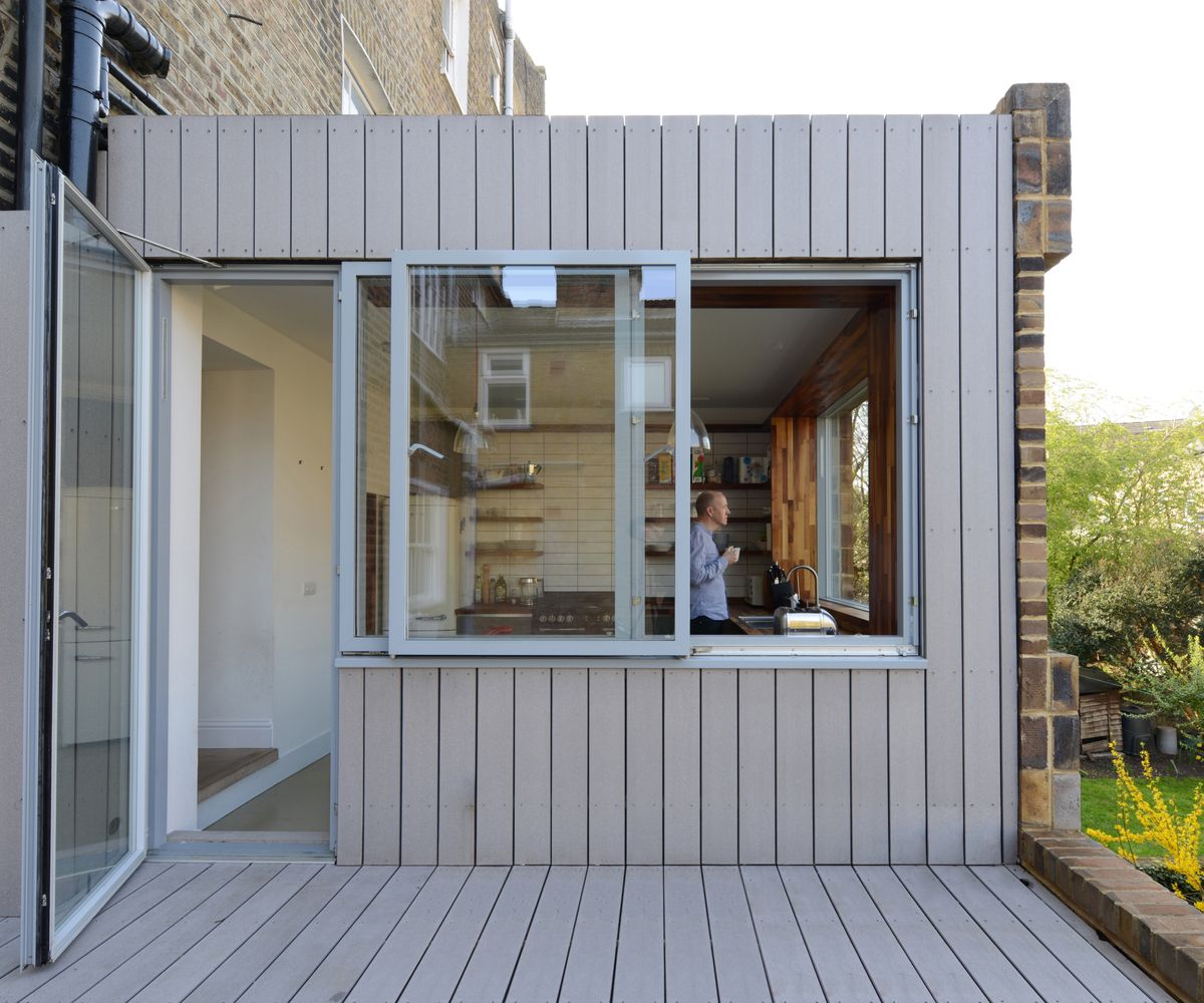 side view of timber clad extension with large pivot door, sliding kitchen window and brick facade to front