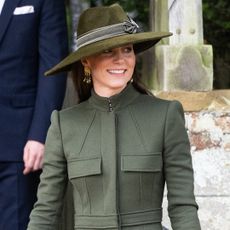 Kate Middleton wearing a green coat and hat smiling and looking to the side