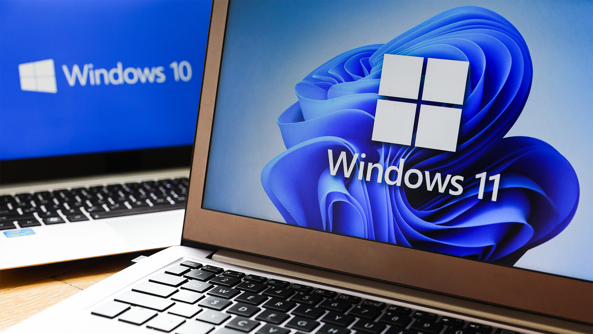 Laptop with Windows 11 logo and branding pictured on screen and second laptop in background with Windows 10 logo and branding pictured on screen.