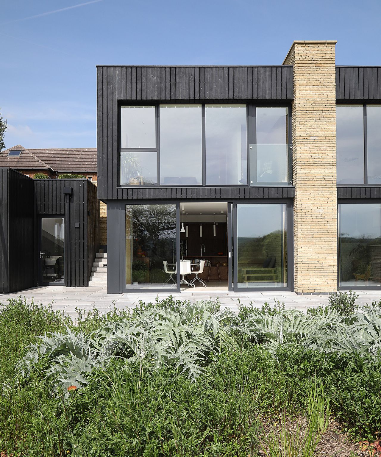 A contemporary self build home with two levels clad in dark timber with large glazing and a brick pillar support