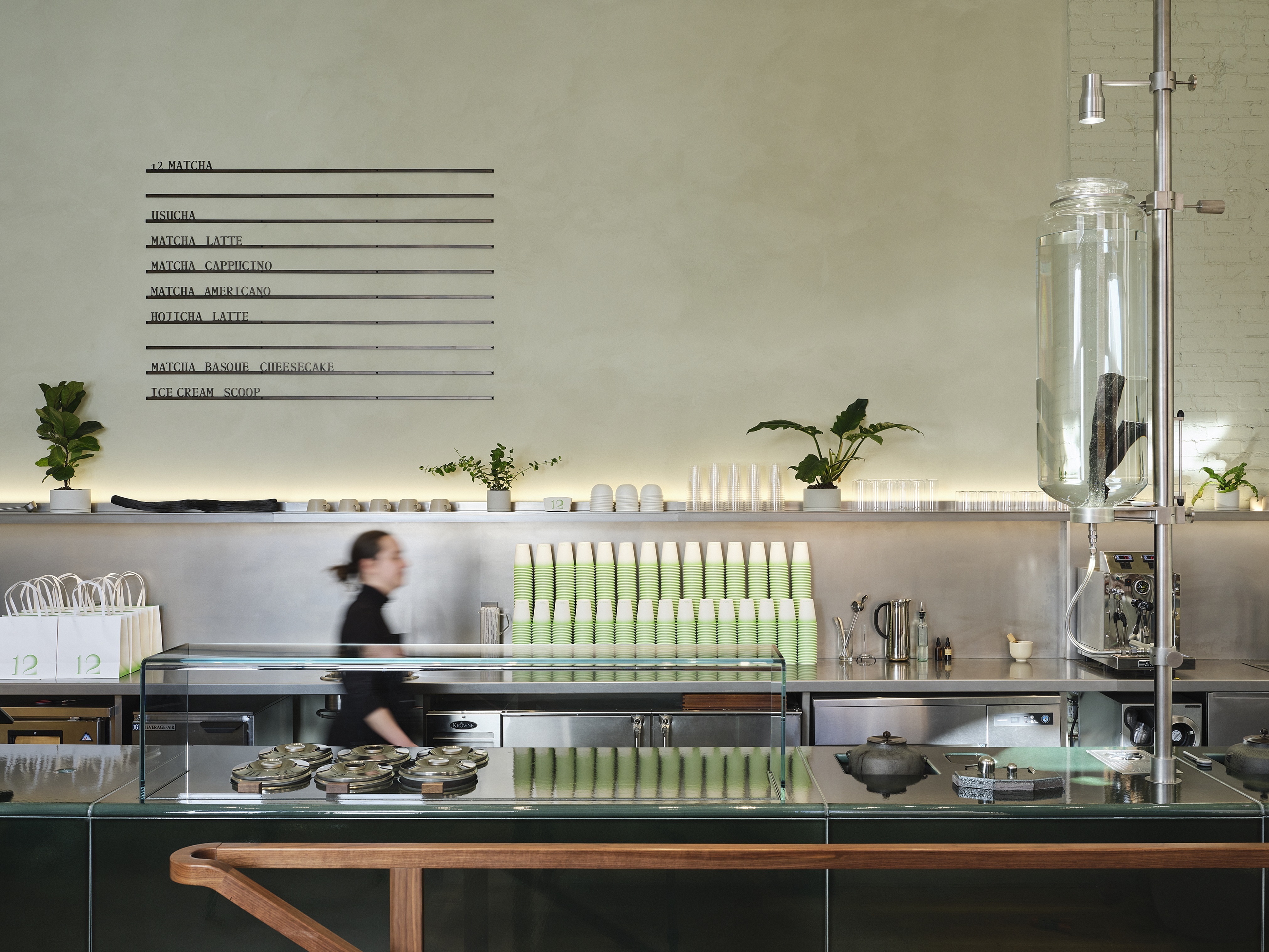 A futuristic matcha cafe with chrome, wood, and green-tinted decor, a dripping water bottle, and matching merchandise.