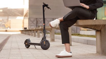 Man sitting on a bench on his laptop, next to an Xiaomi electric scooter
