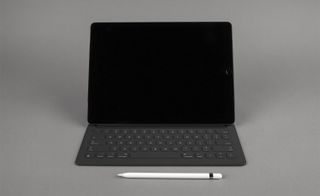 View of an Apple Pencil in front of an iPad Pro which is connected to a Smart Keyboard - all are pictured against a grey background