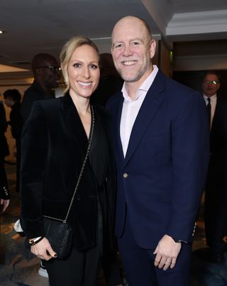 Zara Tindall wearing a black blazer smiling and standing next to Mike Tindall in a blue blazer