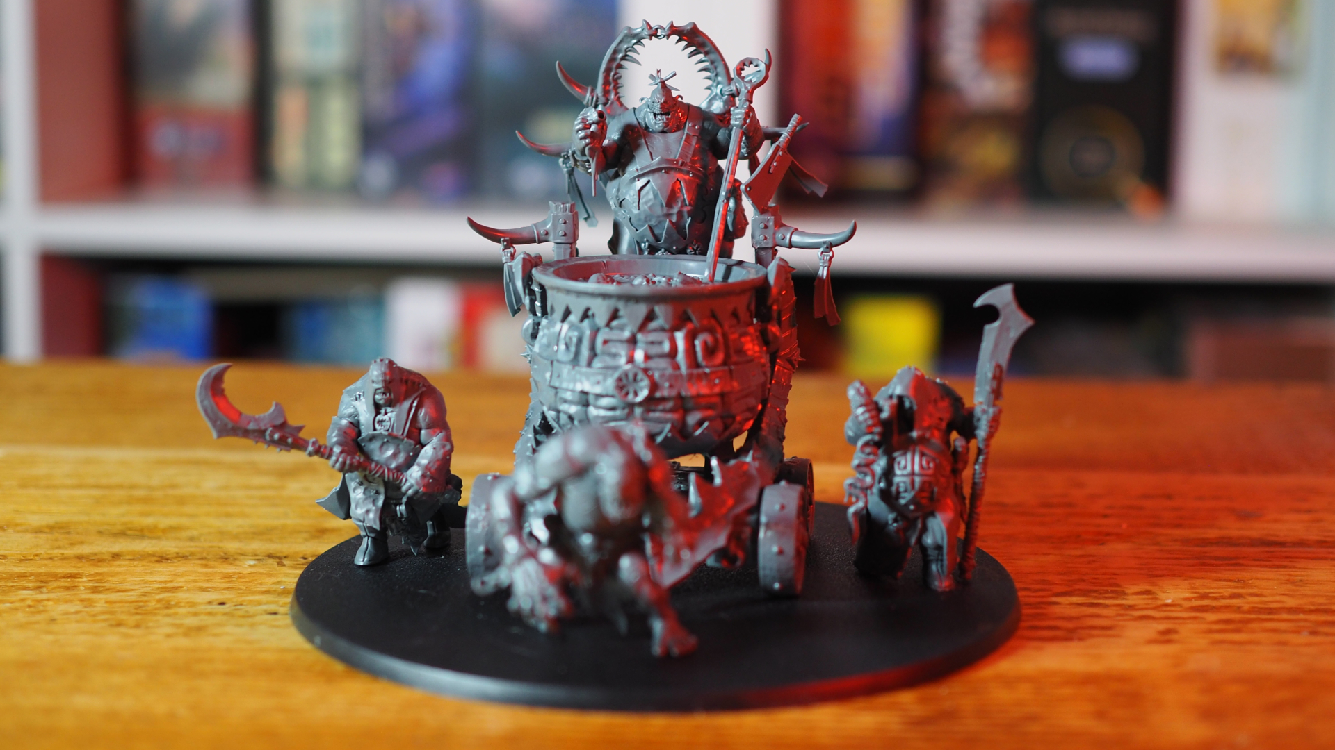 Redd the Maw model on a wooden surface, with blurred board games visible on a shelf in the background
