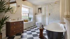 A bathroom with black and white chequered floor tiles, a large tub, a wooden vanity, and a walk-in shower