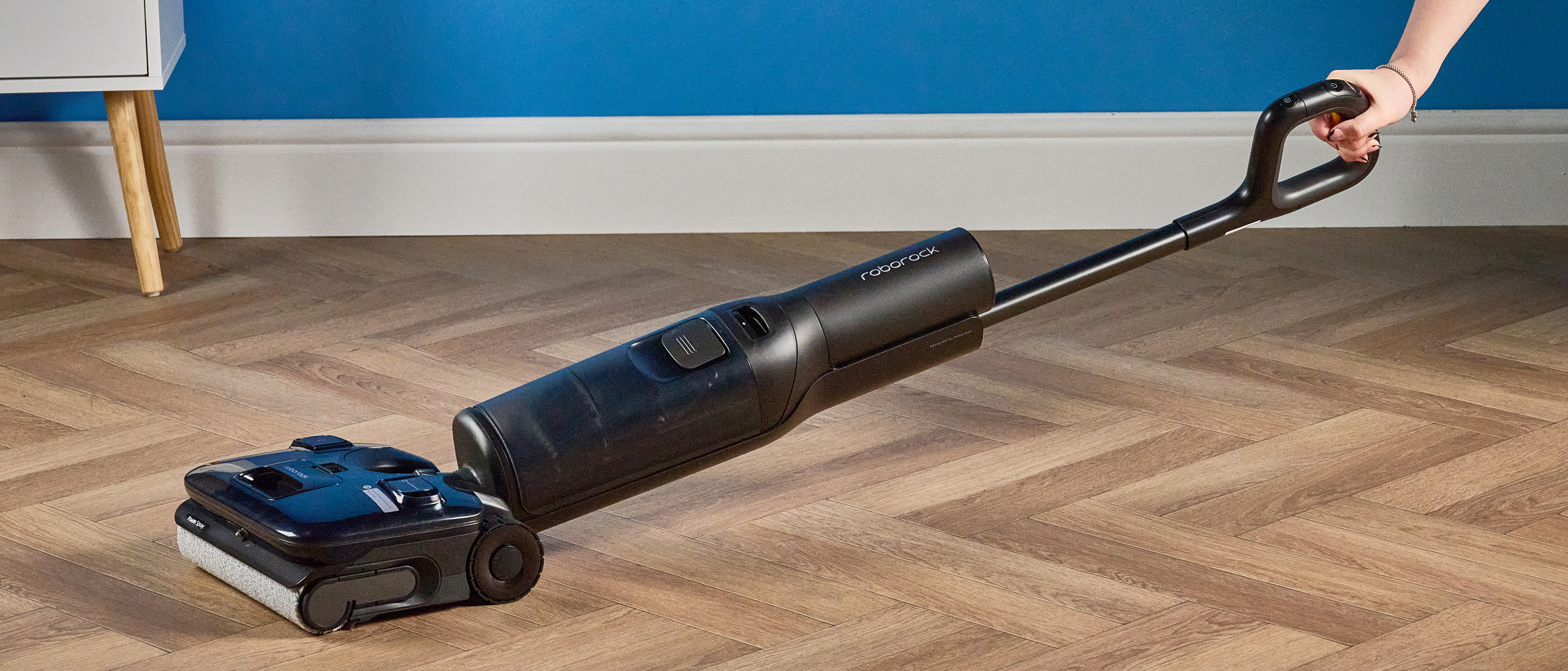 Roborock F25 ACE Pro photographed in front of a blue wall on a wooden floor