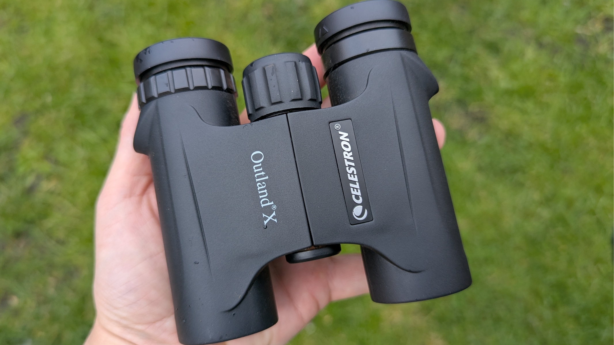 Celestron Outland X in the hand of the reviewer with green grass in the background