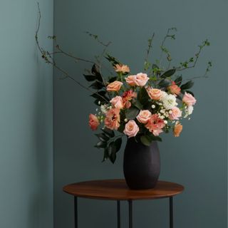 A dark blue room with a wooden side table and a vase of flowers