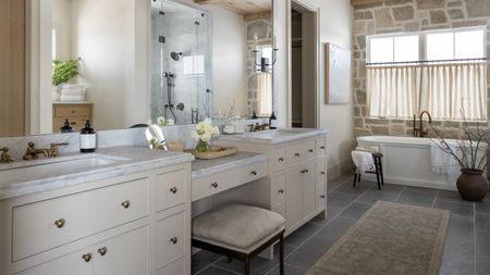 Bathroom with ivory painted double vanity with stool, runner on tile floor, and freestanding bathtub