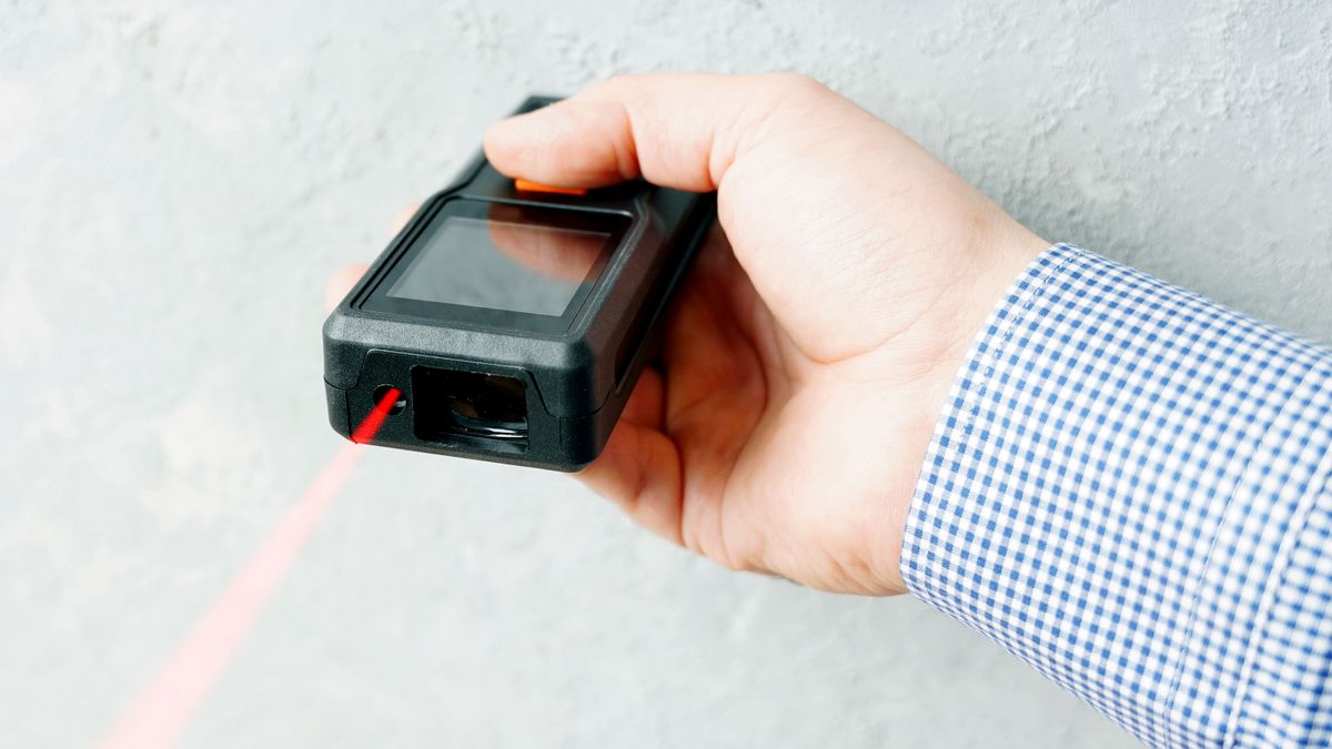 Laser tape measure in hand against white wall