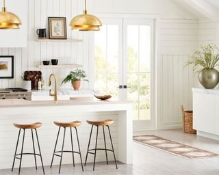 white kitchen with paneled walls, gold pendant lamp, light brown bar stool and rustic decor