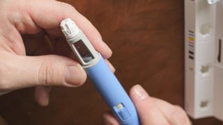 close up of a hand holding a medical device, that being a pen designed to inject the user with the weight loss drug Semaglutide