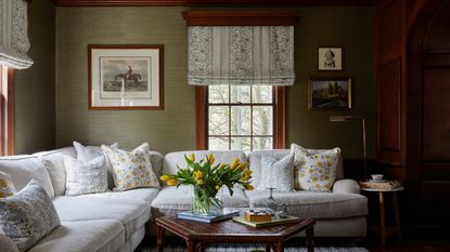 living room with green grasscloth walls, wooden fireplace wall, cream sectional and patterned pillows and blinds