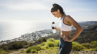 A runner stops above the coast to drink water from a bottle