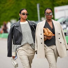 two stylish women wearing tan clothes and sunglasses on a street
