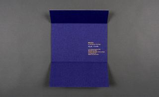 A nondescript cardboard exterior folded open to reveal Prada’s deep blue invitation.