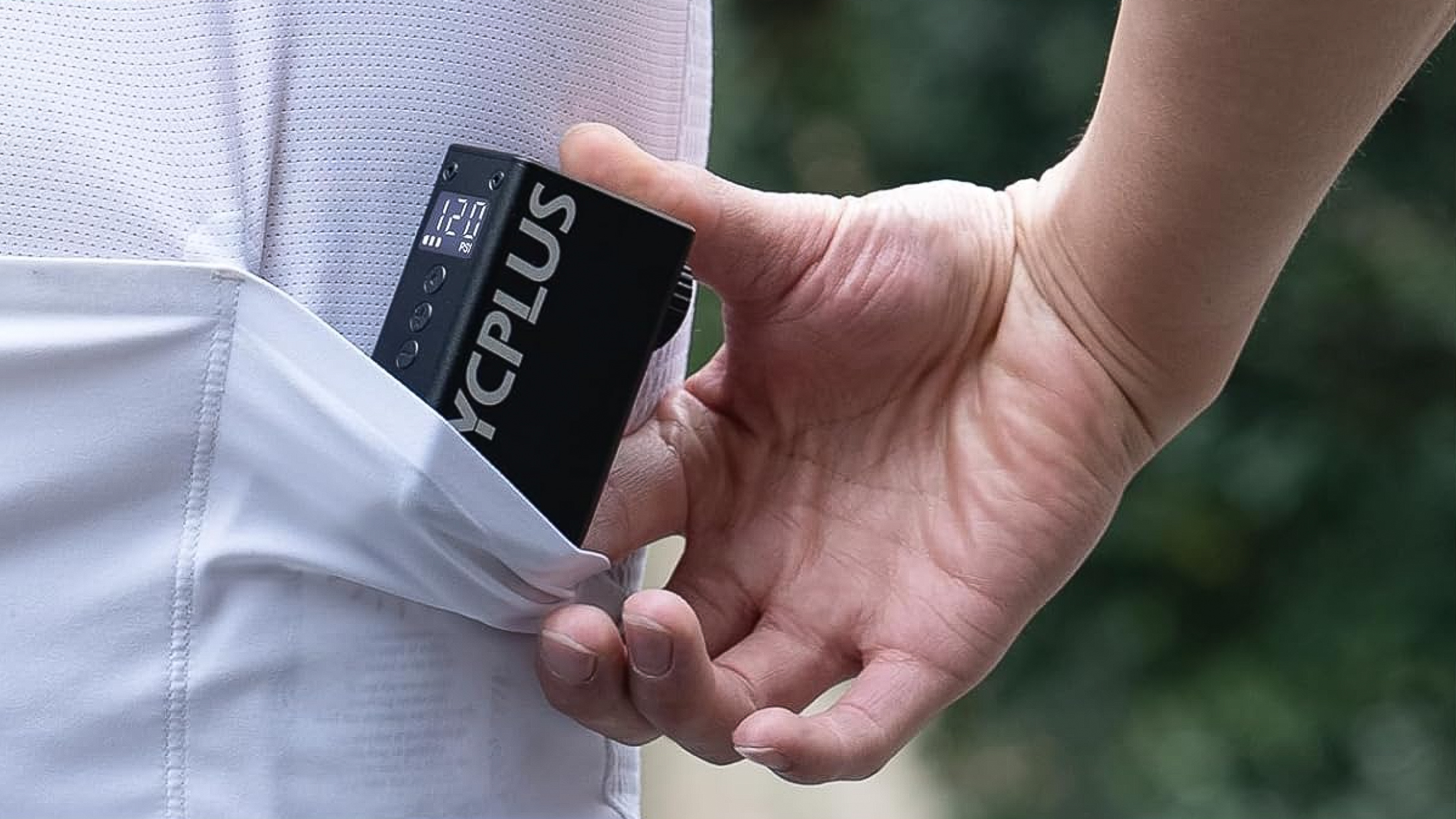 The Cycplus AS2 Pro being slipped into a cycling jersey pocket showing its compact sizing.